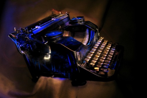 Antique black typewriter painted with UV light. Various objects on a dark background. Artistic blur.